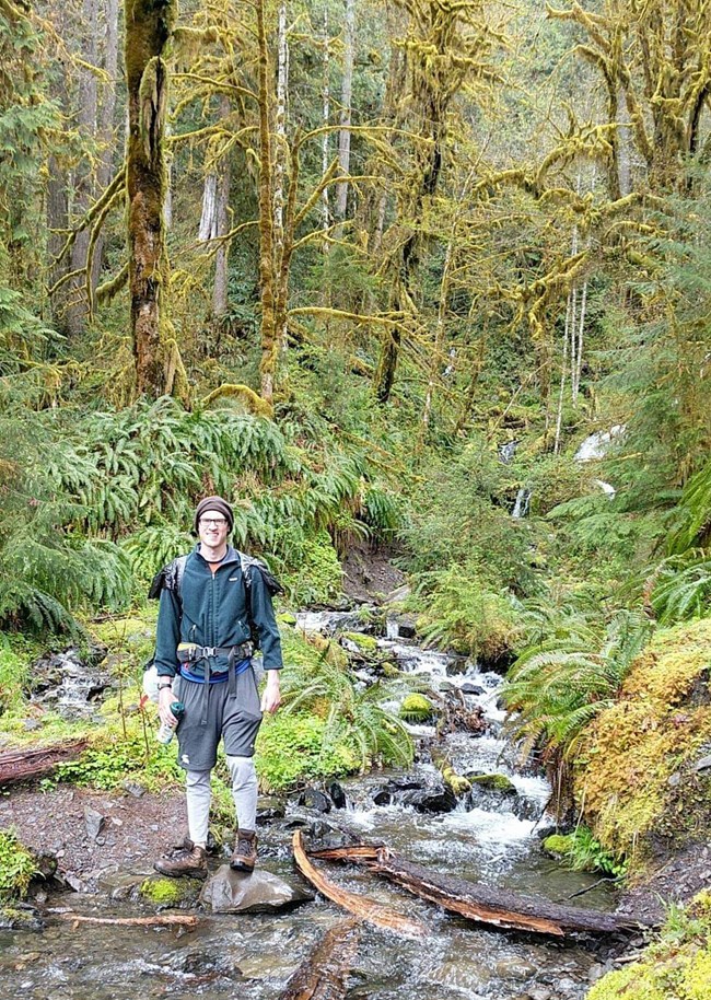 a man stands by a forest stream