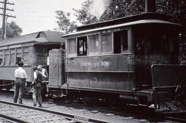 A black and white photo of a steam engine train with people standing around it.