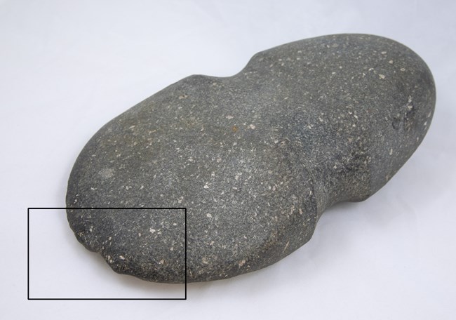 Dark gray, oval-shaped stone with concave groove down center and a black box highlighting the tip.