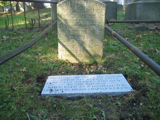 Light grey cemetery stone on ground, with inscription, vertical white stone behind it