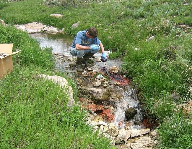 a scientist pouring red dye into a small prairie stream
