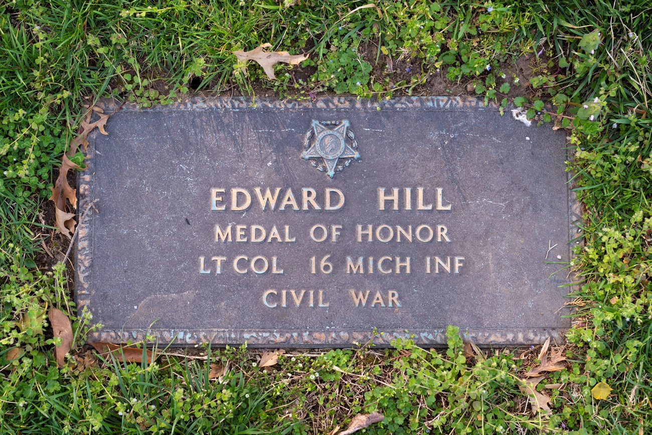 A rectangular burial marker, dark stone, flush with the ground, for Captain Edward Hill.