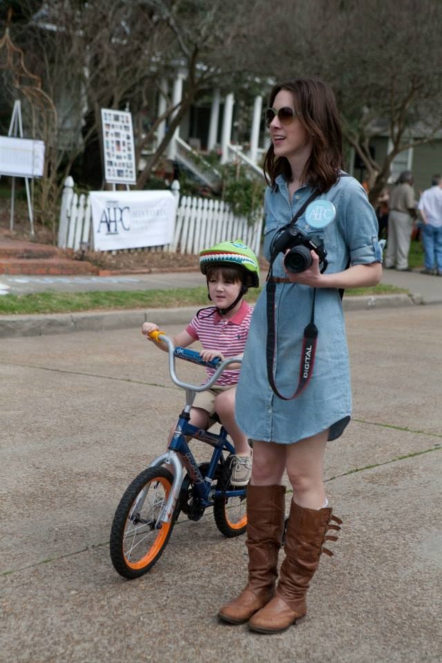 Historic House Fair 2013: A mother with a helmeted child on a bike riding down a festive street.