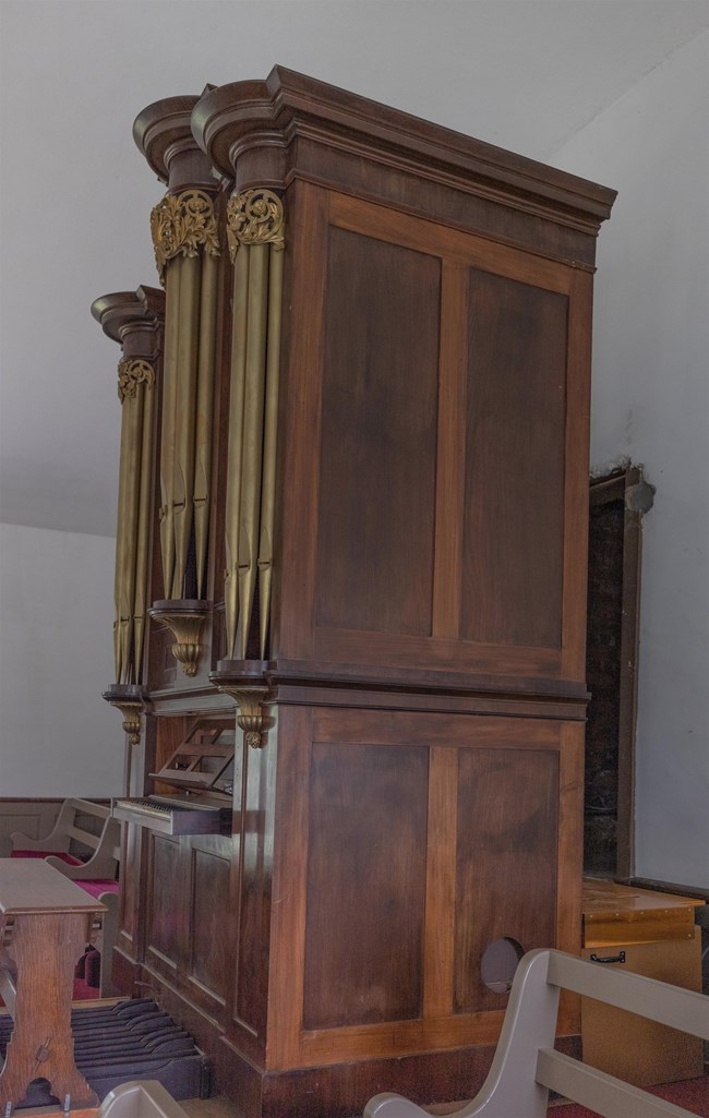 wood paneled organ, with keyboard, located in a church gallery