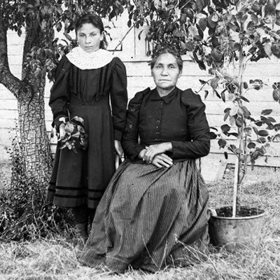 Dated black and white portrait of seated woman and young girl standing in front of house