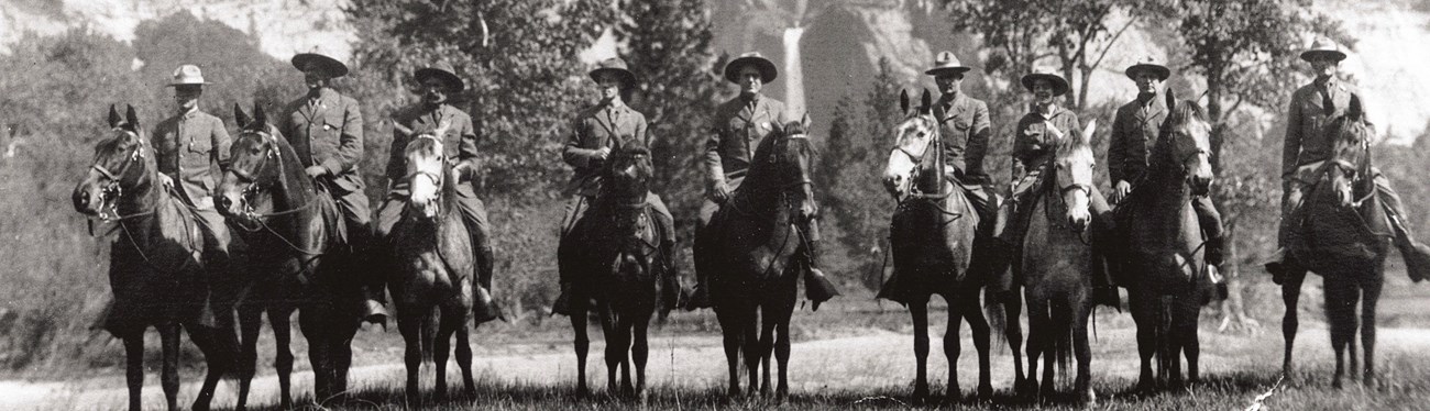 Clare Hodges rides astride her horse with nine uniformed mounted patrol rangers.