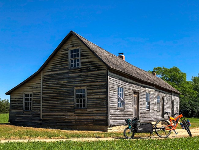 An orange bicycle sits next to a historic wooden barn.