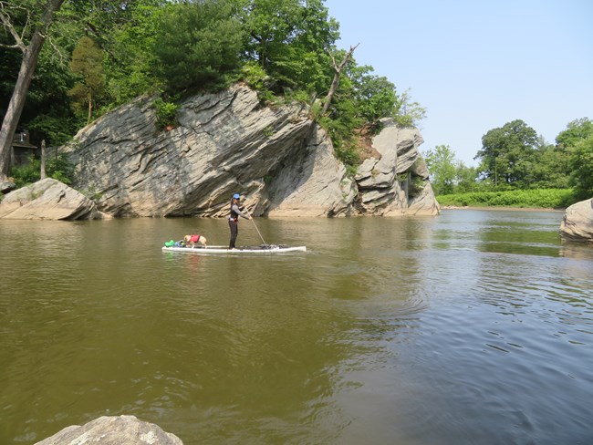 A person paddling on the water with large rocks in the background.