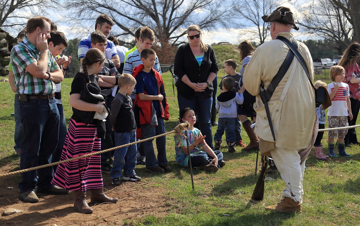 a ranger in 18th century clothing speaks to children and adults seated and standing