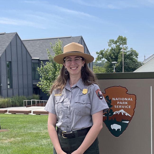 Allison Horner-Peters a woman wearing a NPS ranger uniform stands in front of a sign