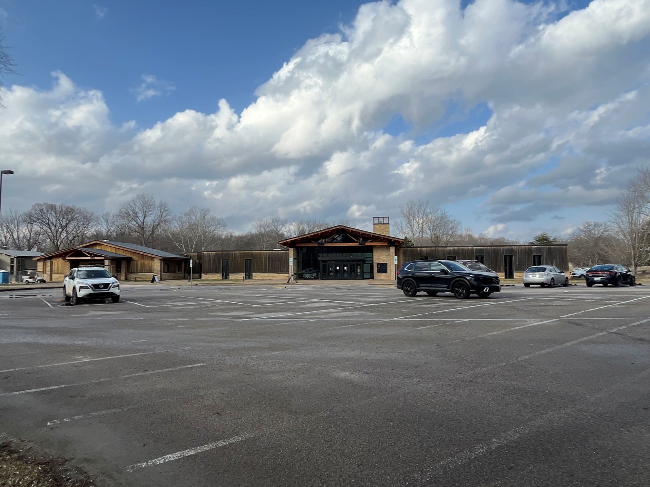 A parking lot with scattered cars against the background of a large stone and wooden building.