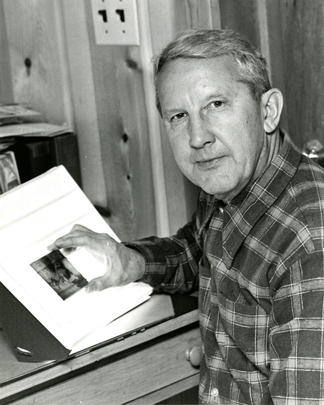 Man in a plaid shirt sitting at a light table holding a glass slide