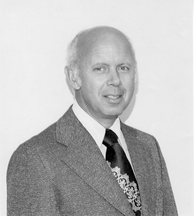 Howard Chapman in a suit and tie poses for a photograph.