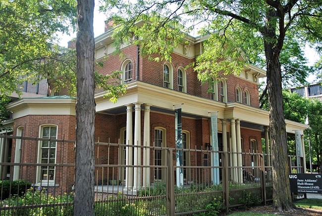 Hull_House,_Chicago,_IL by Elisa Rolle CC BY SA Brick exterior of Hull House surrounded by trees