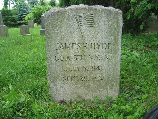 Grayish gravestone, with inscription and a flag, set in a cemetery