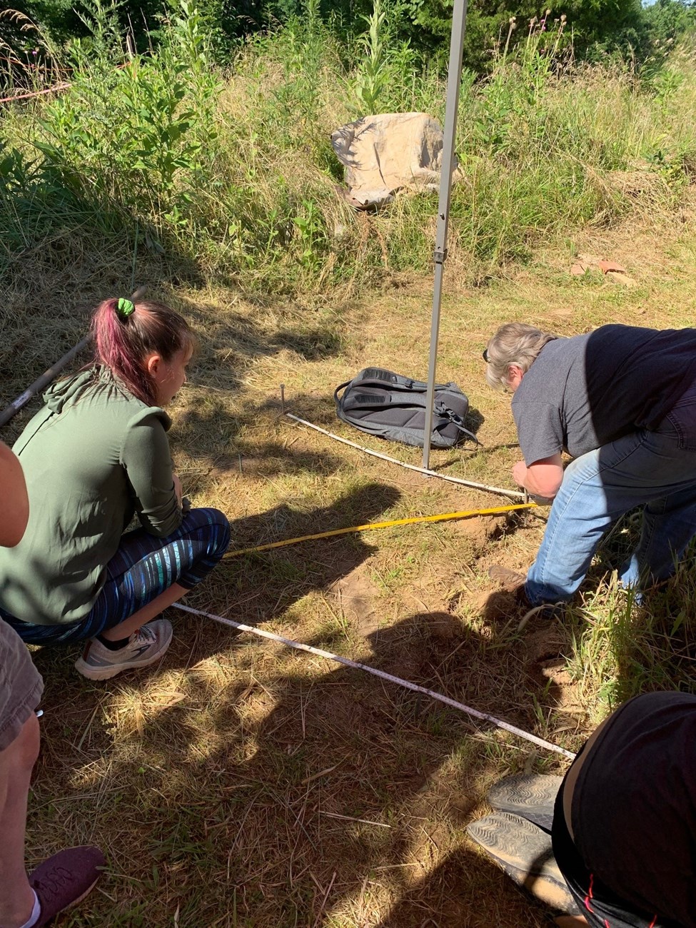 IG Story Photo 2 - Oldham County Takeover the Network A high school student watches as an experienced archaeologist begins to dig in the ground.