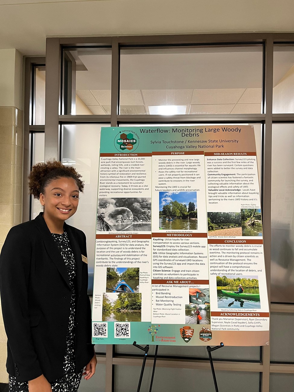 Sylvia Presenting Her Work A woman stands in front of a poster with information.
