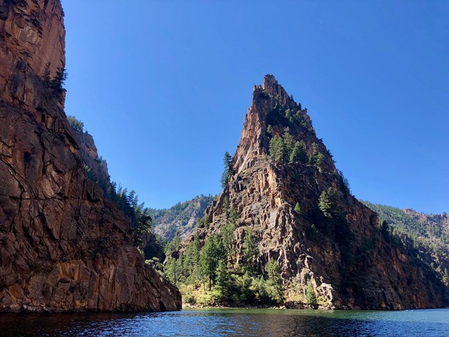 A tall pinnacle of rock standing offset from surrounding canyon walls. Water flows beneath the walls.