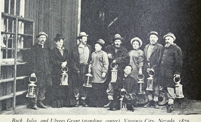 group of people wearing large coats and holding lamps. Text reads "Buck, Julia, and Ulysses Grant (standing center). Virginia City, Nevada 1879."