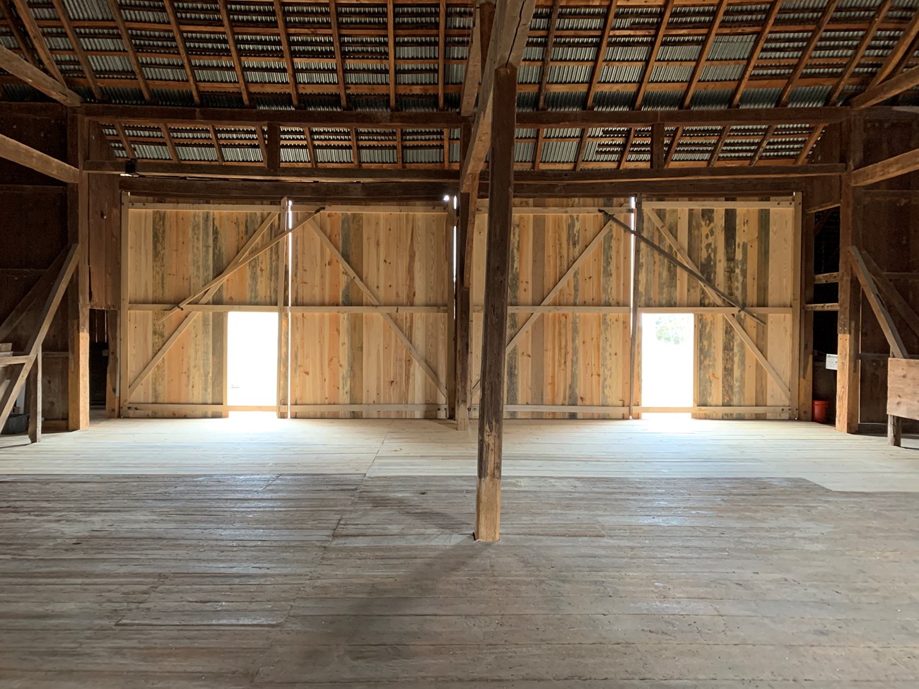 Inside a historic wooden barn. Large open interior with two smaller doors on the far wall. The doors are inset in full-wall sized barn doors.