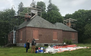 two individuals confer outside of brick museum with scaffolding on it