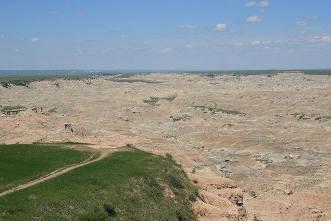 vast badlands formations sprawl into the far distance, surrounded by green grasslands