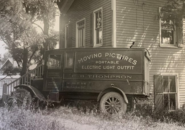 Old style van parked in front of a house. Van signed for E.B. Thompson photography and motion pictures