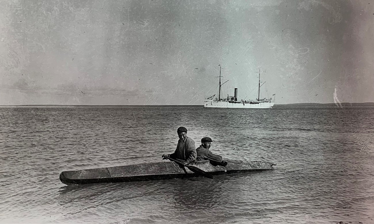 Two men in a sea kayak with a large boat in the background