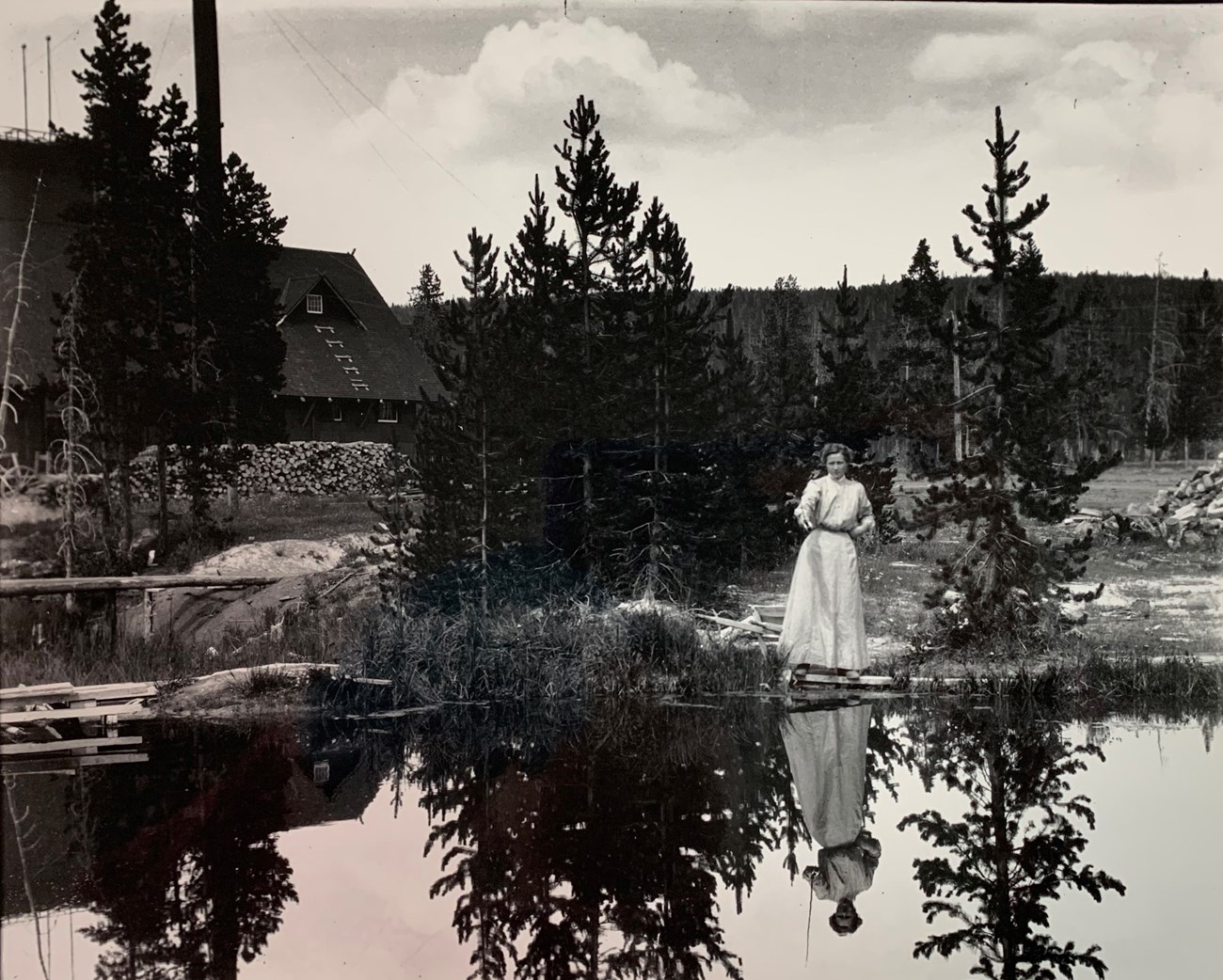 Woman in a long dress fishing in a lake with a large building behind