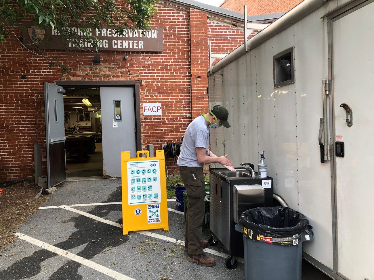 A worker wearing a cloth mask washes their hands in a mobile handwash station sink in a rolling cart.