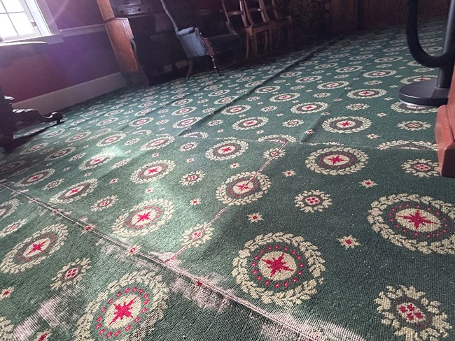CFH 3 R A close-up photo of the Douglas Sitting Room carpet in the Chief Factor's House. The carpet is threadbare and rippling due to water damage.