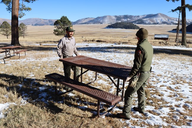 Two maintenance workers move a picnic table.