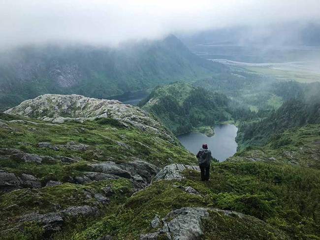 A woman walks in a foggy fjord landscape.