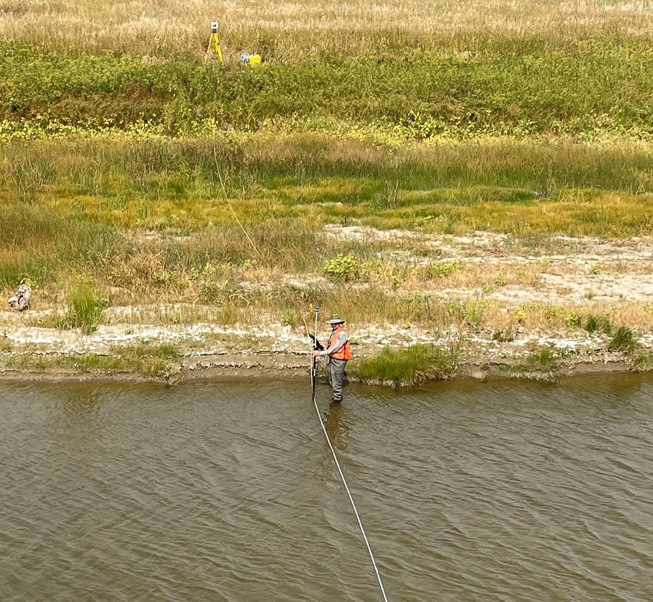 man in a river with tripod in the distance