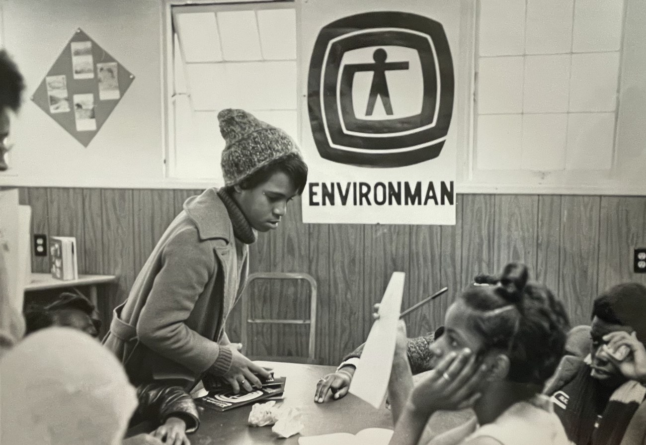 Teacher and students at a table with large Environman poster on the wall