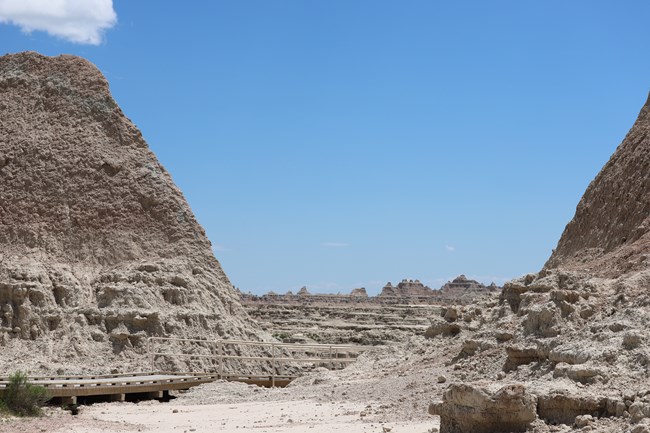 a boardwalk path goes through a low point between two buttes with badlands formations beyond the low point