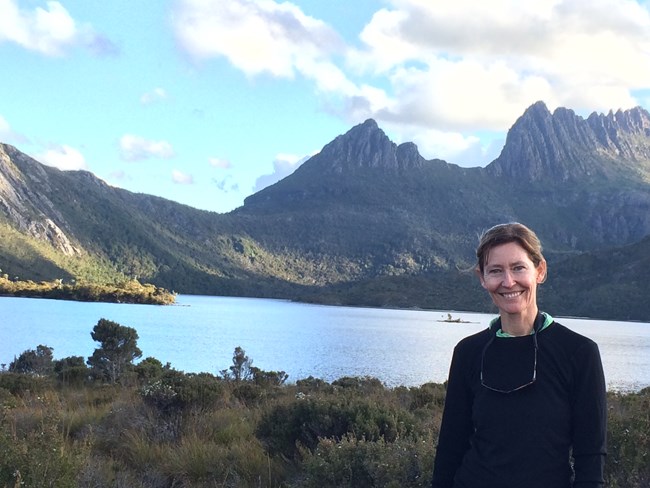 Woman stands in front of remote lake with view of rugged mountains in background.