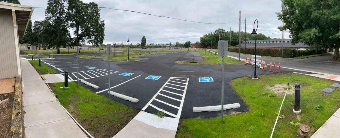Crossroads Lot A parking lot with numerous accessible parking lots is shown, along with a sidewalk, small landscaped areas, and the corner of a grey building.