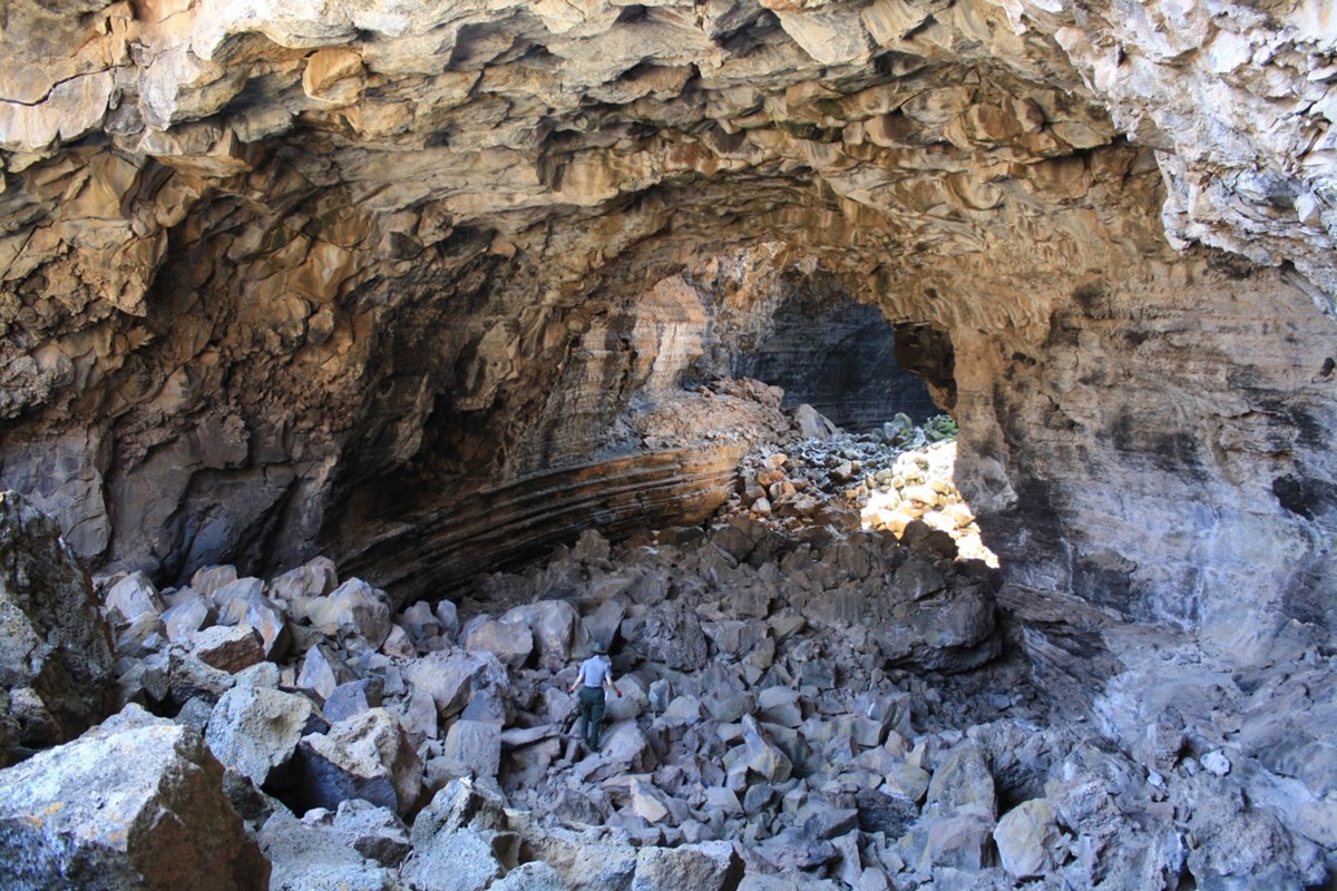 Photo of a ranger climbing over boulders on the floor of a large lava tube cave