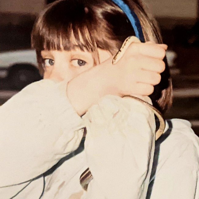 Rachel as a young girl, peeking over her arms at the camera as she holds up a garter snake.