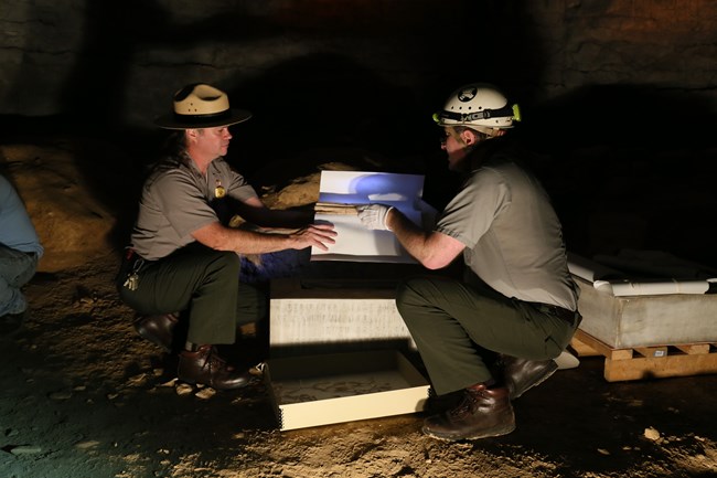 Two park rangers hold a collection of historic papers over a stone box.