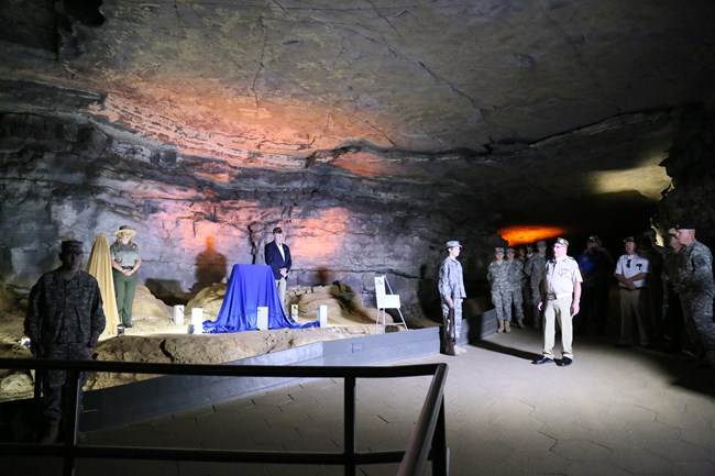 A group of veterans, military, and park rangers gather for a dedication ceremony in the cave.