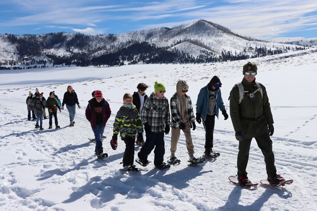 A park ranger leads a group of students on a snowshoe hike.