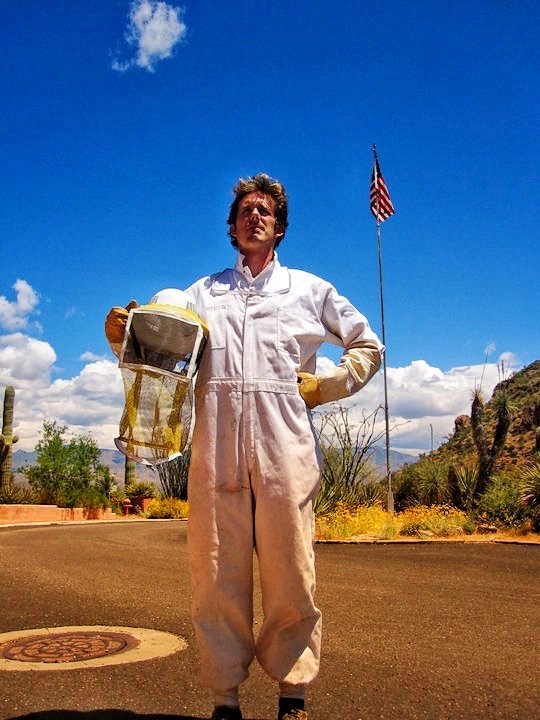 A man in a white suit and holding a bee keepers helmet
