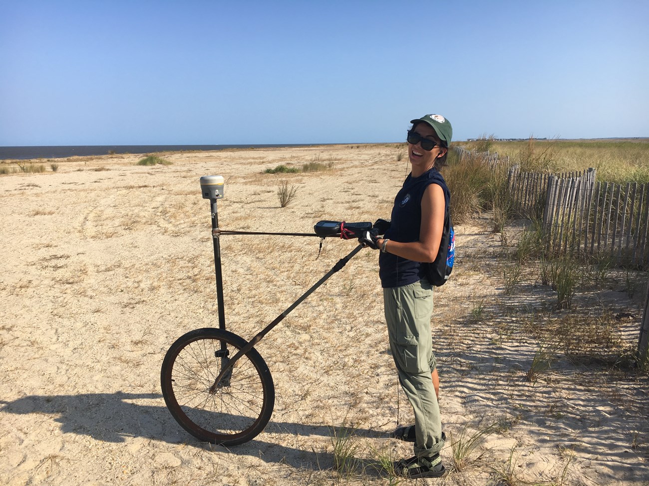 intern stands on a beach with a GPS tool that looks like a bike.