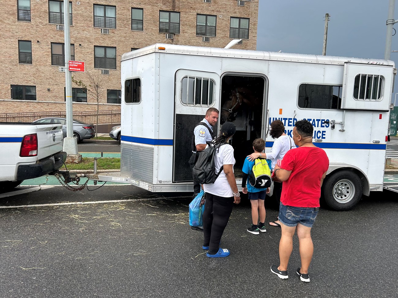 U.S. Park Police Horse National Night Out A U.S. Park Police Officer in uniform stands in front of a horse trailer with a black horse's head visible while a child and three adults watch.