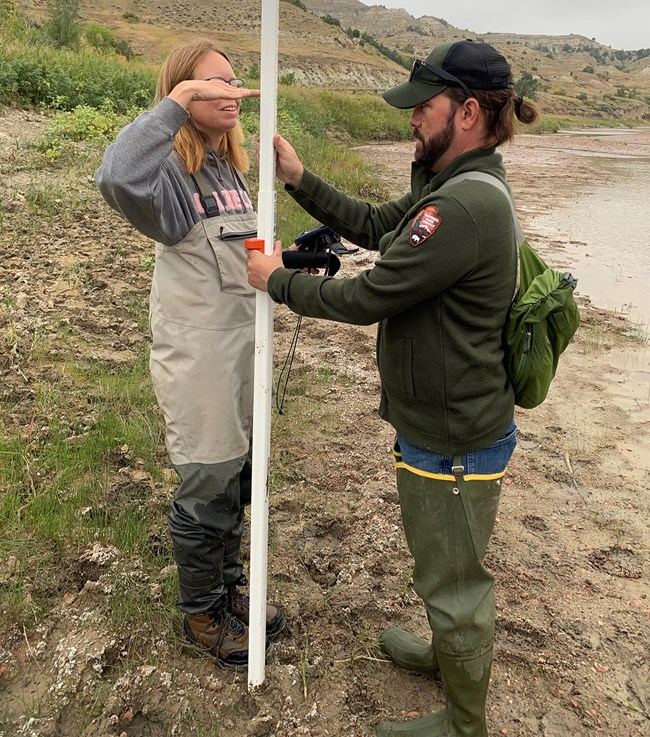 Stream monitoring at KNRI man and woman holding a tall measuring stick