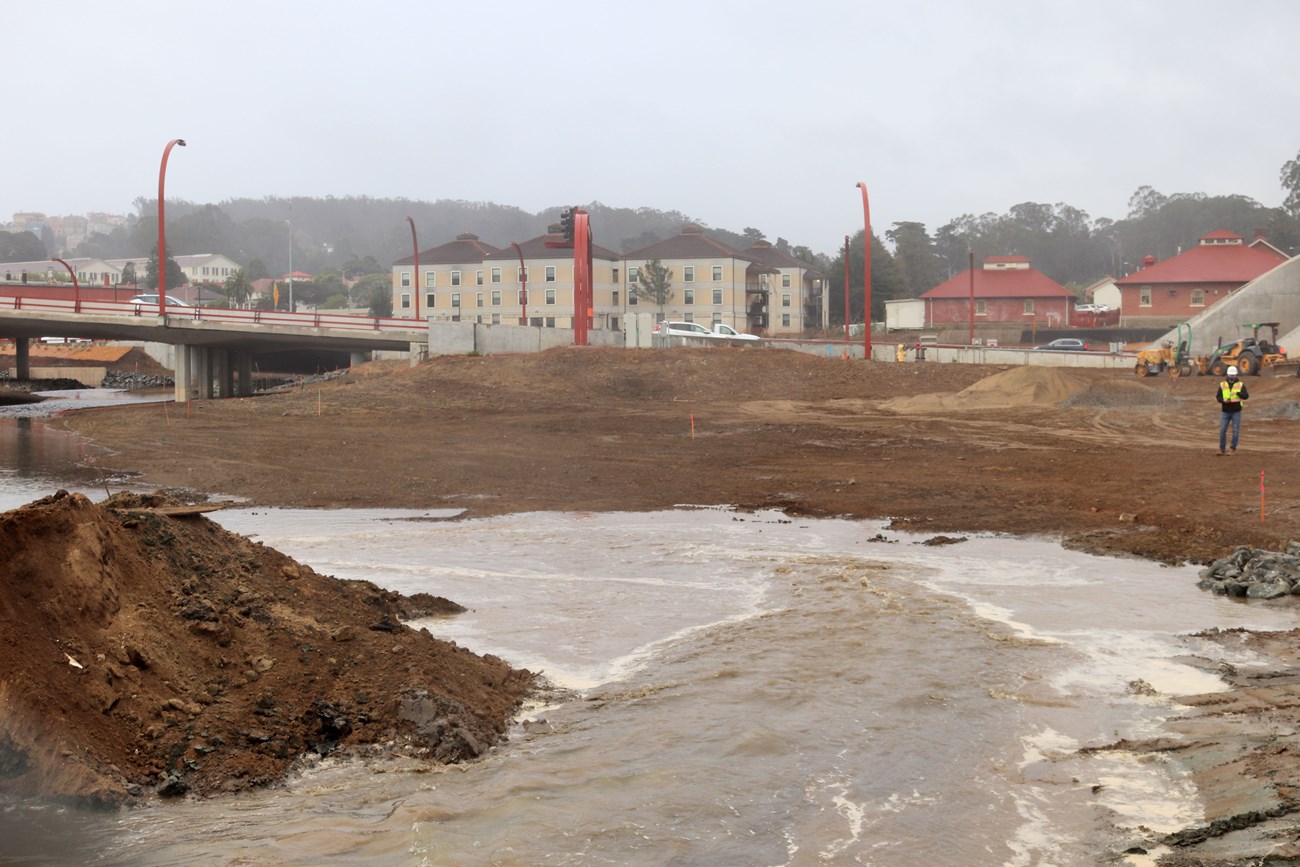 Berm removal On a gray day, water rushes between freshly moved piles of earth.