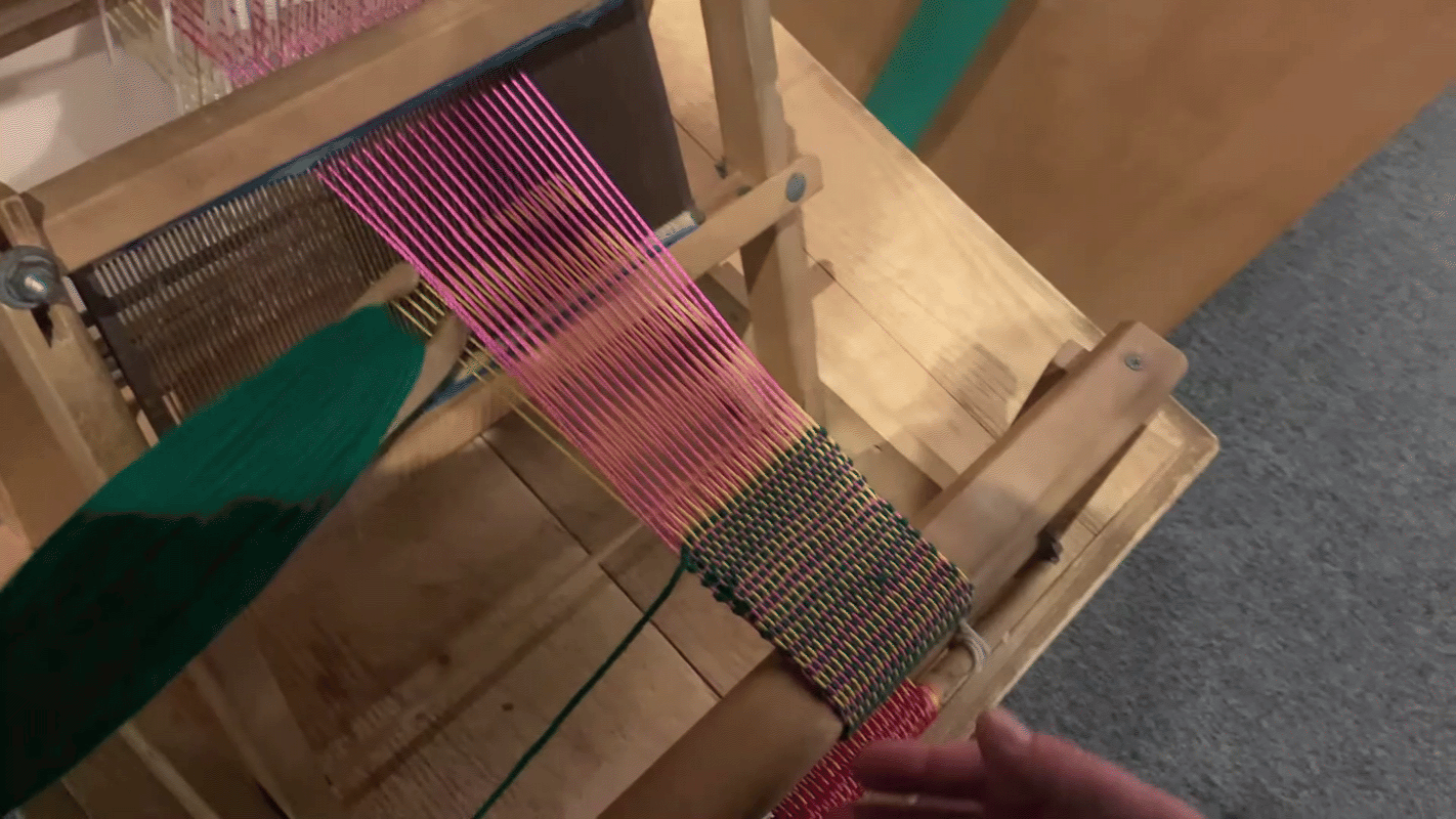 picking gif green yarn is passed through a "V" shaped opening of yellow and pink yarn