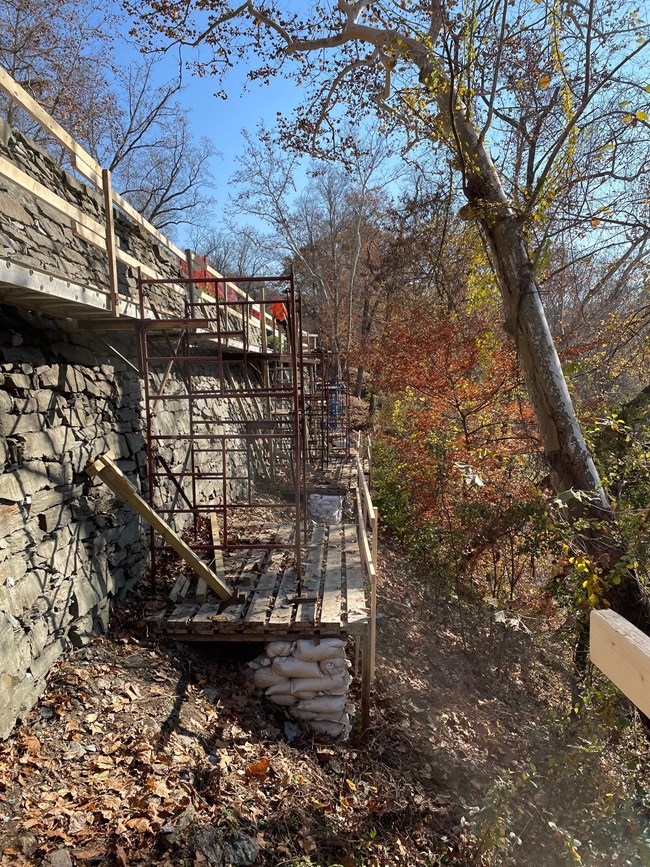 A large stone wall has scaffolding beside it to allow for repairs